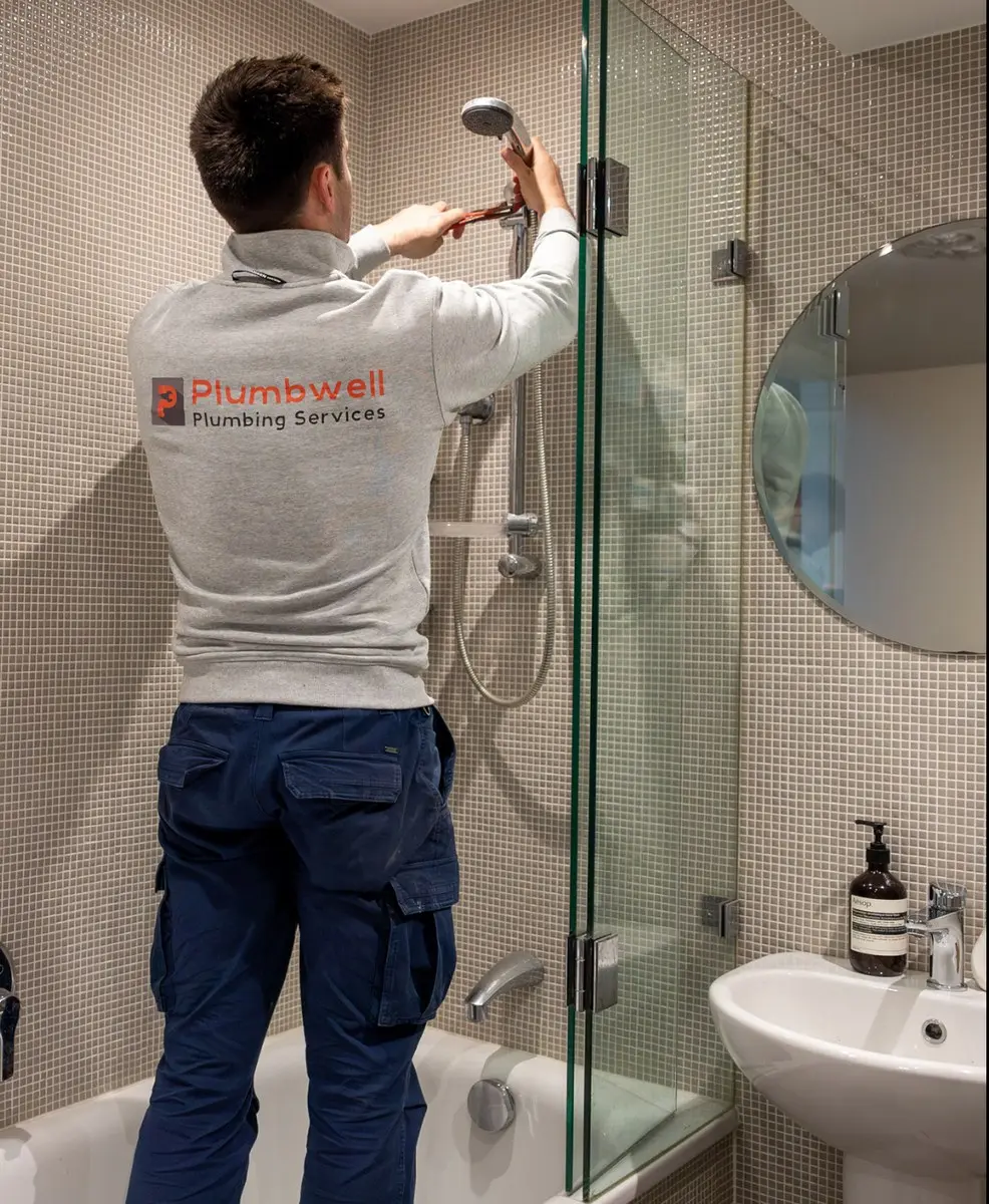 A Plumbwell plumber fitting a shower head in a tiled bathroom